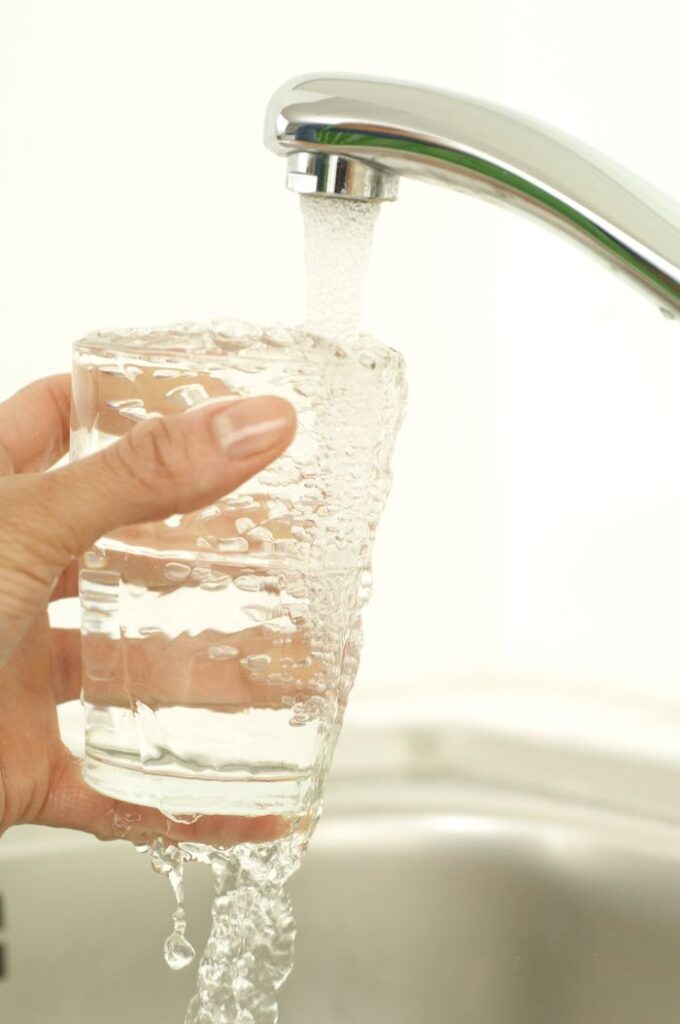 Close-up of a hand holding a glass as tap water fills it, promoting cleanliness and freshness.